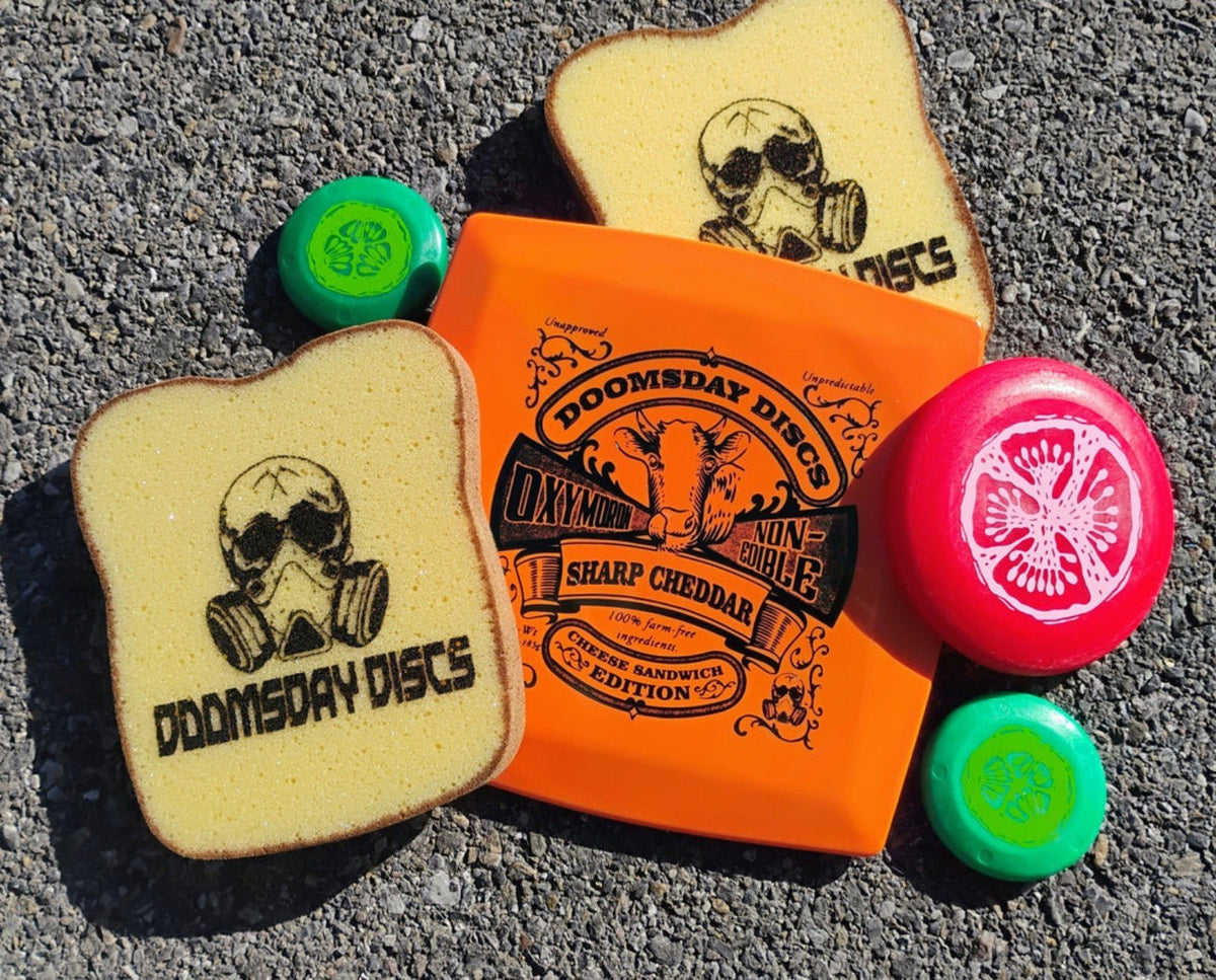 Complete Oxymoron Cheese Sandwich Edition set with orange Survival Sharp Cheddar disc, two bread sponges, two green pickle minis, and one red tomato mini